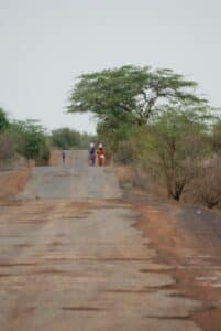People walk on a rural road carrying things.