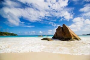 brown rock formation on sea shore under blue and white sunny cloudy sky during daytime
