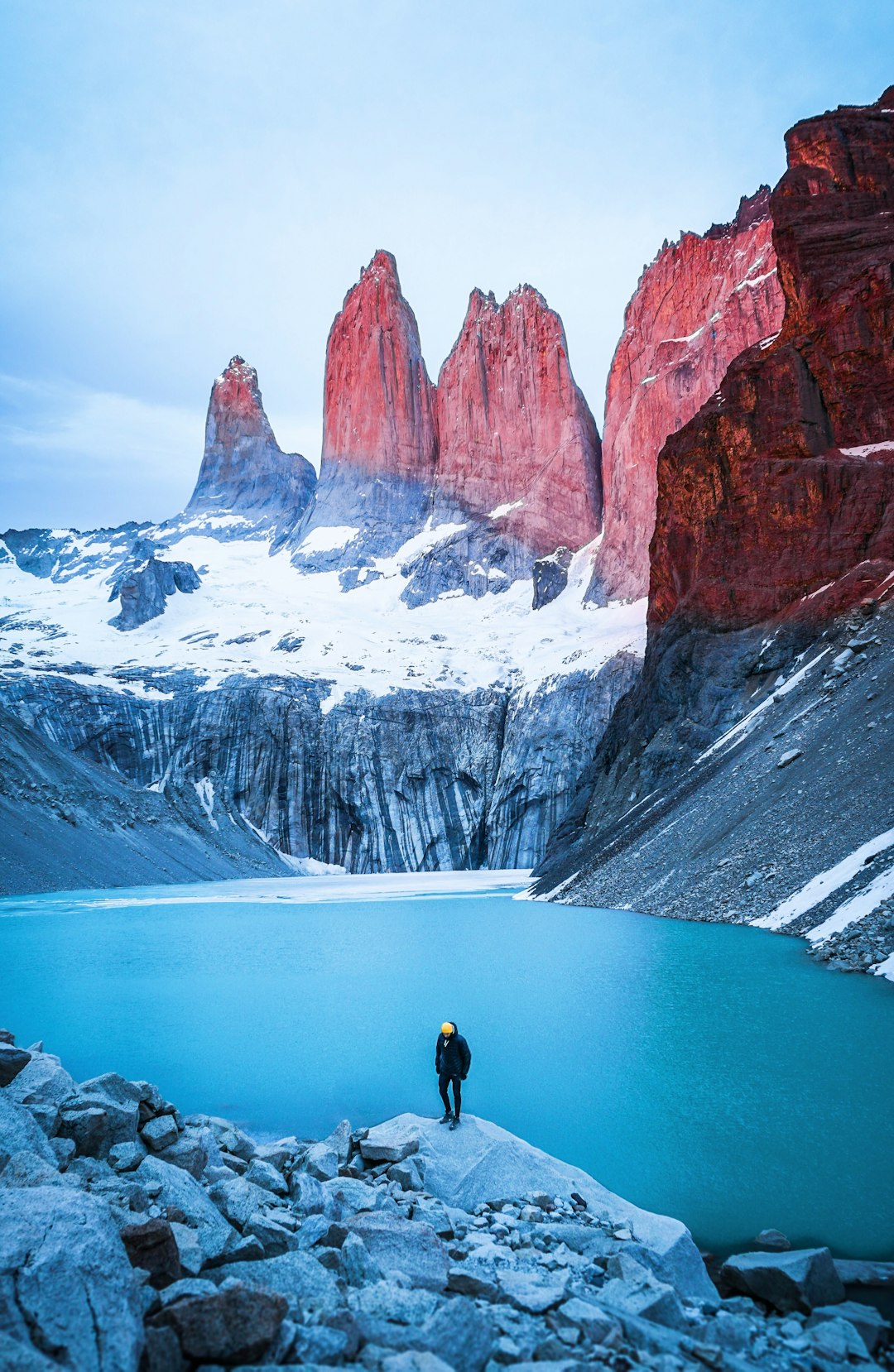 Photo by Samuel Chenard man standing on rock facing body of water and mountain